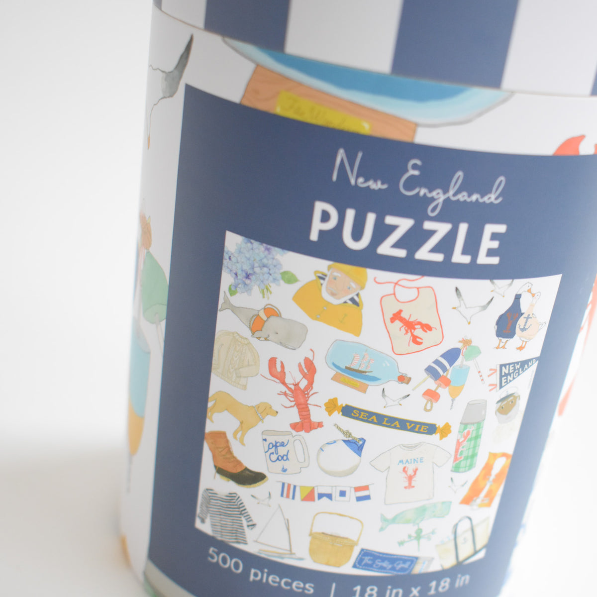 Cylindrical container for a 500-piece New England Puzzle featuring a nostalgic collage of illustrated icons including a whale, lobster, lighthouse, and nautical motifs.