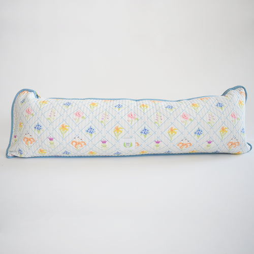 The Sara Fitz Lumbar Pillow, Cross Stitch Floral, is a long, rectangular cotton quilted pillow made in India with a white background, blue edging, and a grid of colorful floral and small motif designs.