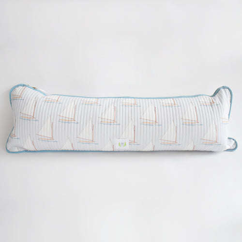 The Sara Fitz Lumbar Pillow, Sailboat, is a long rectangular cotton quilted pillow with a white cover featuring sailboats, blue piping, and a plush down alternative insert. Made in India. Shown on a plain white background.