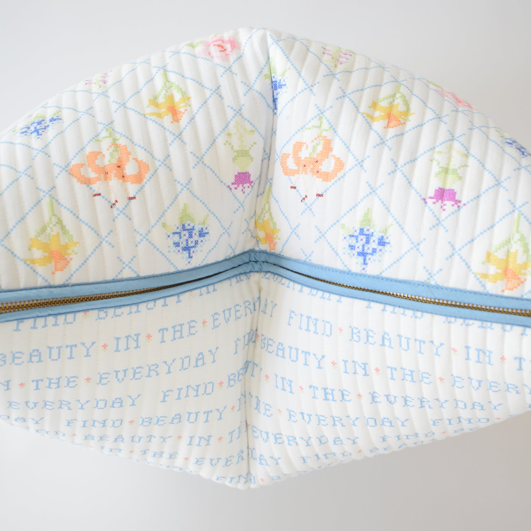 The Sara Fitz Oversized Pillow features a cross-stitch floral pattern on white, with an inspiring "FIND BEAUTY IN THE EVERYDAY" message in blue and orange repeated on the lining. Made in India.