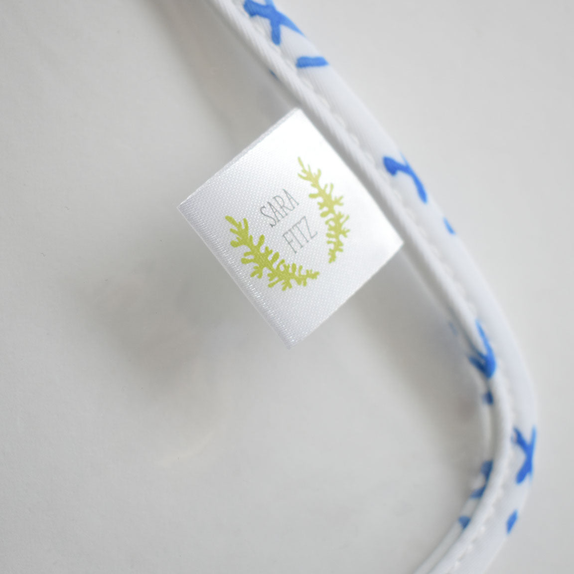 The Anchor Project Bag by Sara Fitz is a white heavyweight canvas bag adorned with blue anchor patterns and a sewn-in Sara Fitz tag framed by a green leafy design. Shown against a white background, it’s ideal for fans of distinctive Sara Fitz prints or anyone in need of an oversized project bag with style.