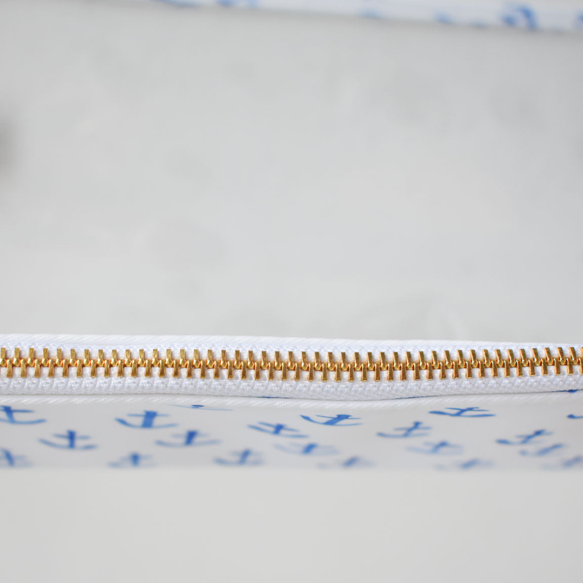 Close-up of the gold zipper on the white heavyweight canvas Anchor Project Bag by Sara Fitz, featuring blue anchor patterns inspired by classic Sara Fitz prints, with a softly blurred background.
