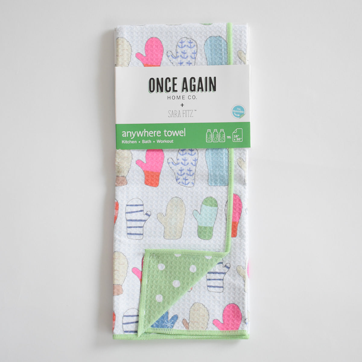 Folded white Sara Fitz Anywhere Towel, Mittens, featuring a colorful pattern of mittens, a green-and-white polka dot corner, and absorbent fabric.