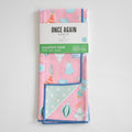 A folded Sara Fitz Anywhere Towel, Ornament featuring a Christmas ornament pattern on absorbent fabric with a light green polka-dot underside, secured with a product label.