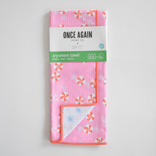Sara Fitz Anywhere Towel, Peppermint, featuring a pink repeating peppermint candy pattern with an orange trim, wrapped in a Once Again Home Co. label and made of absorbent fabric.