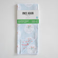 Sara Fitz Anywhere Towel, Happy Snowman, featuring light blue microfiber fabric with a pattern of snowmen in earmuffs and scarves, folded with a branded paper sleeve around the center.