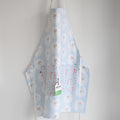 Sara Fitz Attach + Go Apron, Happy Snowman, featuring a light blue pattern of snowmen and candy canes, hanging against a white wall.