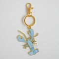 A Sara Fitz Blue Lobster Bag Charm, featuring an imported light blue enamel lobster with gold outlines and a convenient gold keyring clasp, displayed on a plain white background.