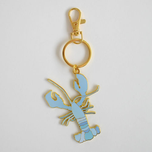 A Sara Fitz Blue Lobster Bag Charm, featuring an imported light blue enamel lobster with gold outlines and a convenient gold keyring clasp, displayed on a plain white background.