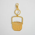 The Sara Fitz Nantucket Basket Bag Charm is a gold keychain featuring a flat, stylized enamel design of a basket with a handle, attached to both a key ring and lobster clasp, shown on a plain white background.