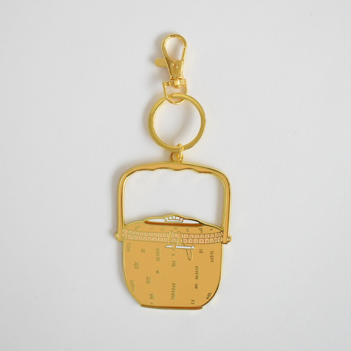 The Sara Fitz Nantucket Basket Bag Charm is a gold keychain featuring a flat, stylized enamel design of a basket with a handle, attached to both a key ring and lobster clasp, shown on a plain white background.