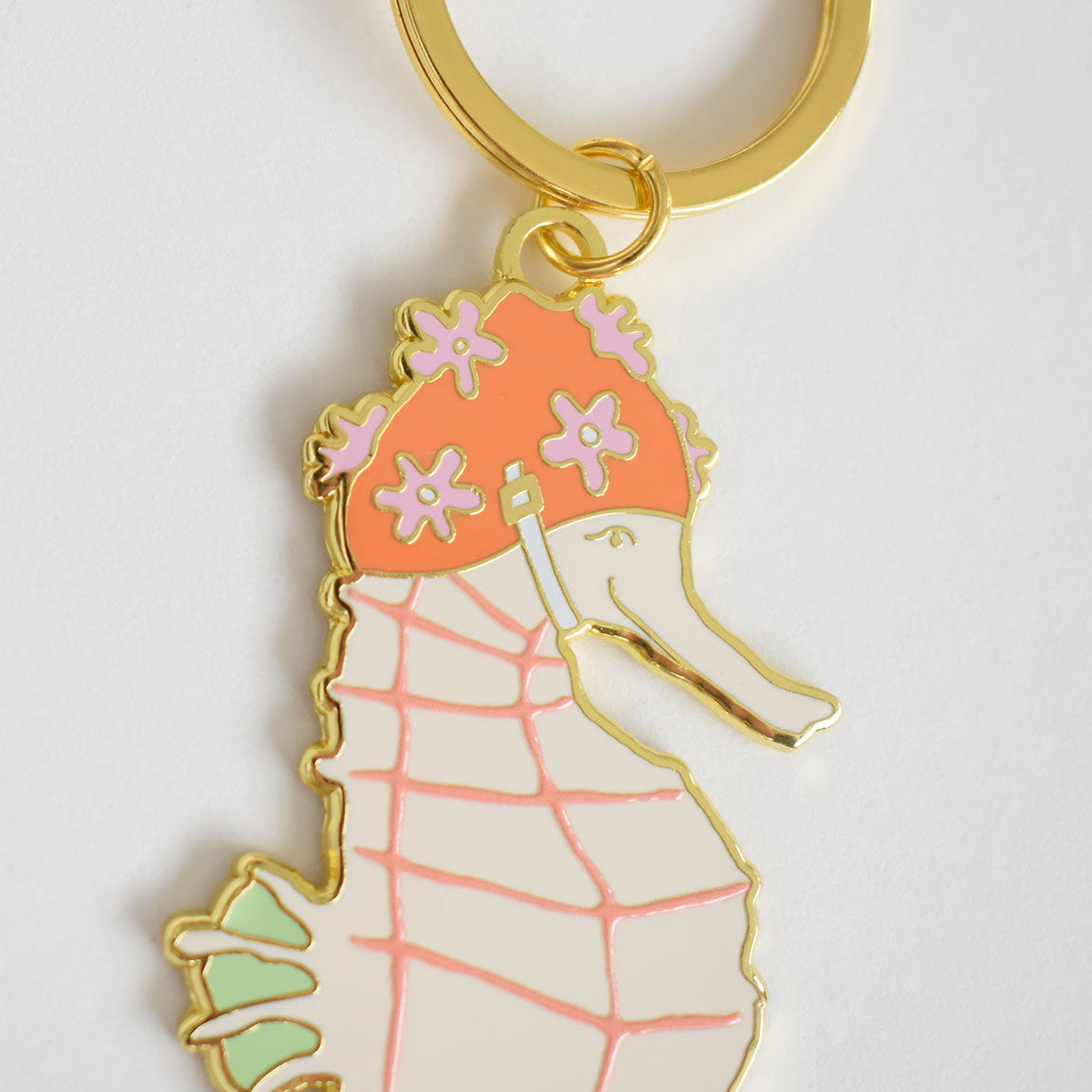 Sara Fitz Seahorse Bag Charm: An imported gold keychain featuring a pastel enamel seahorse wearing a pink flower-adorned shower cap, attached to a sturdy ring.