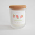 The Berry Picking Candle by Sara Fitz is a 10 oz frosted glass jar with a cork lid, featuring hand-drawn strawberries. Hand-poured in Maine with coconut soy wax, it has notes of strawberry, sugar, guava, and citrus. Plain white background.