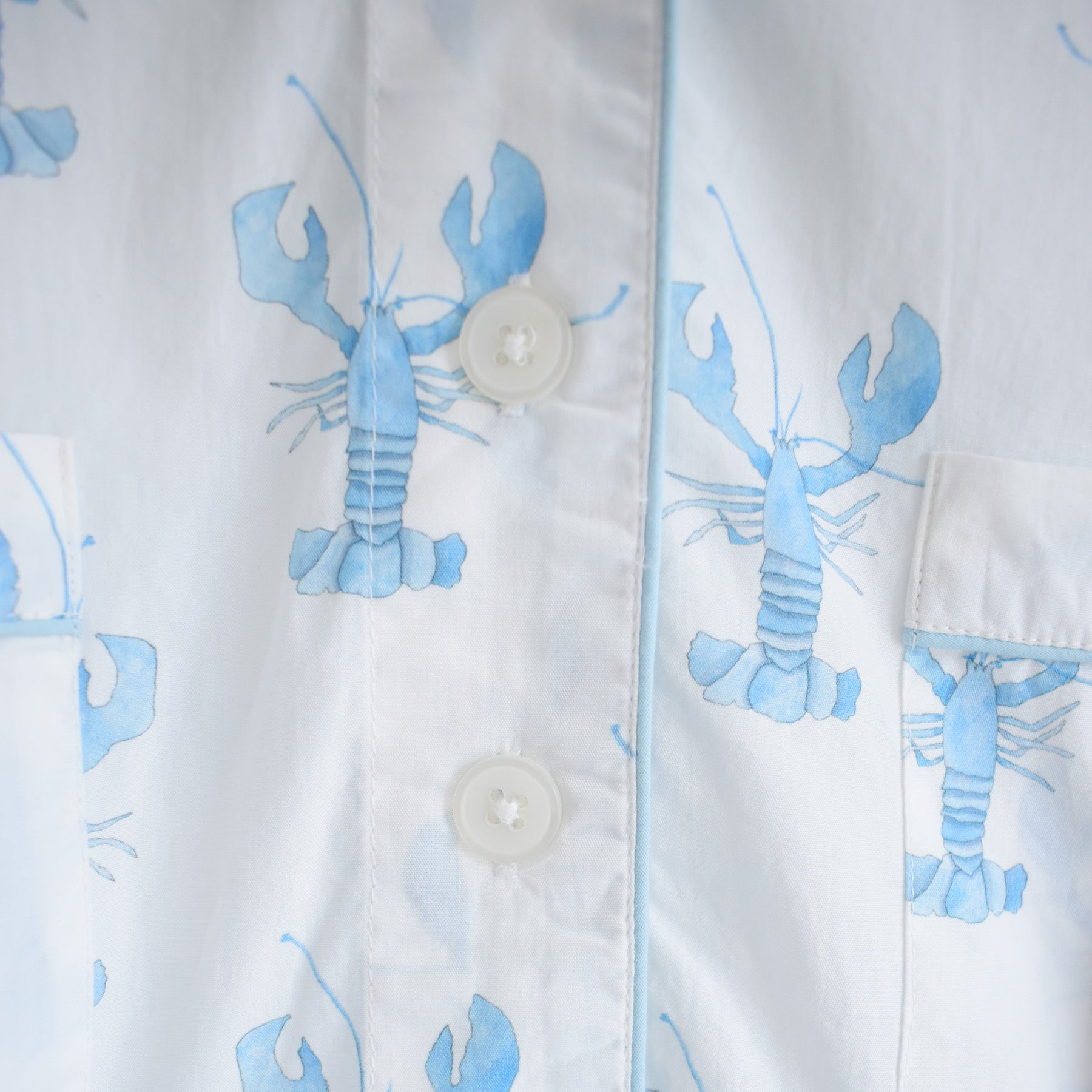 Close-up of the Sara Fitz Blue Lobster Sleep Shirt, showcasing light blue lobster prints on white cotton fabric, accented with white buttons and visible pocket seams—a stylish addition to women’s sleepwear.