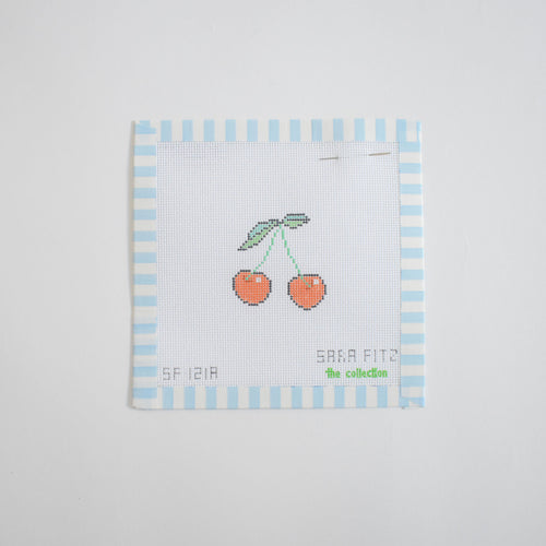 The MINI Cherries Needlepoint by Sara Fitz features two red cherries with green leaves on white fabric, bordered in light blue and white stripes. The 18 mesh stitch-painted canvas has "Sara Fitz" and the collection name printed at the bottom.