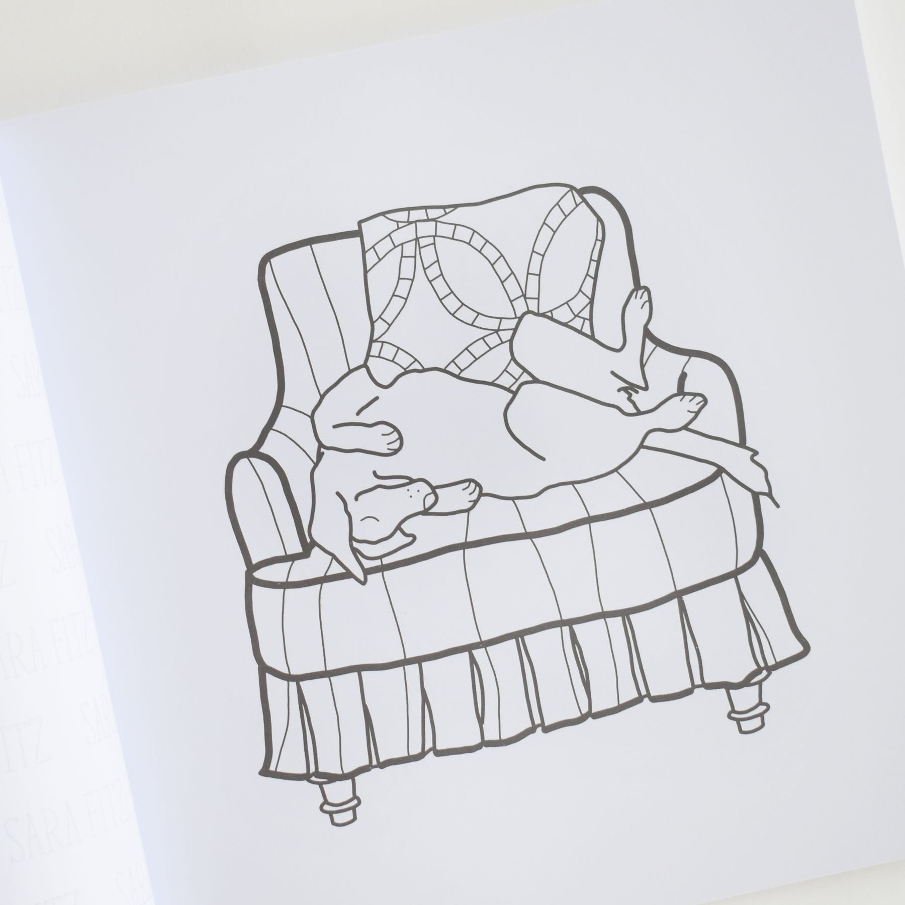 A line drawing from Sara Fitz’s Coloring Book Countryside, depicting a dog sleeping on its back on an armchair with a patterned blanket draped over the backrest—capturing the charming New England illustration style perfect for adult coloring books.