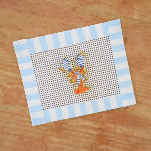 The Sara Fitz "Cozy Lobster Needle Minder" features an orange lobster with a bow on a blue and white striped needlepoint canvas—ideal for pairing with your favorite stitching accessories.