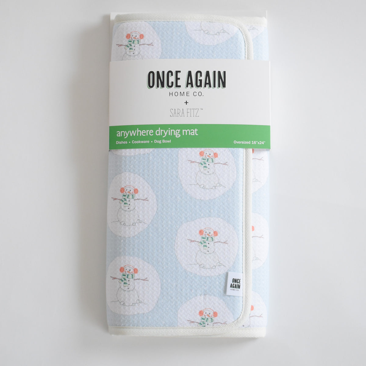 A folded light blue Anywhere Drying Mat, Happy Snowman, featuring a microfiber pattern of snowmen with earmuffs and scarves, held by a product label.