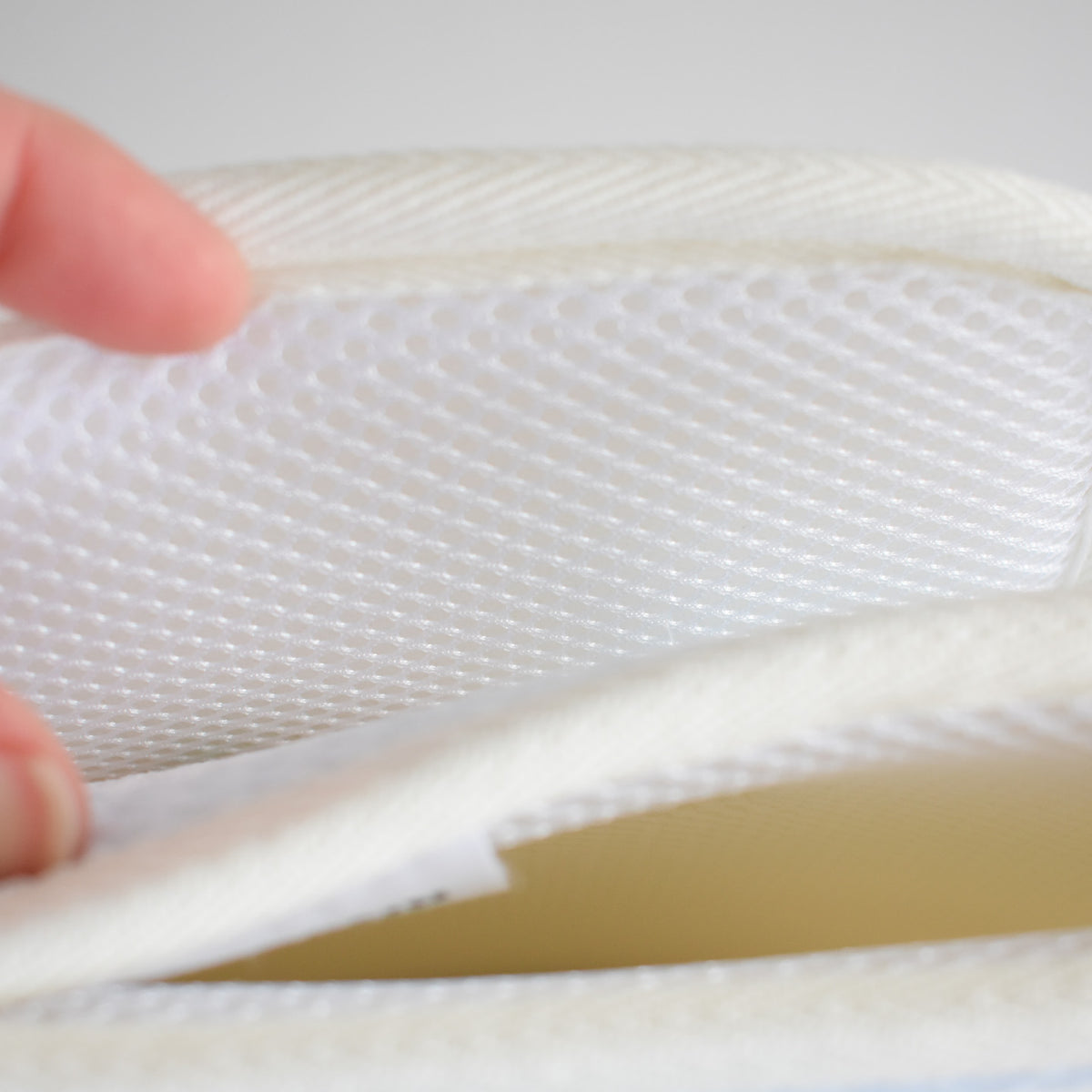 Close-up of a hand lifting the corner of a white Anywhere Drying Mat, Happy Snowman to reveal the foam interior.