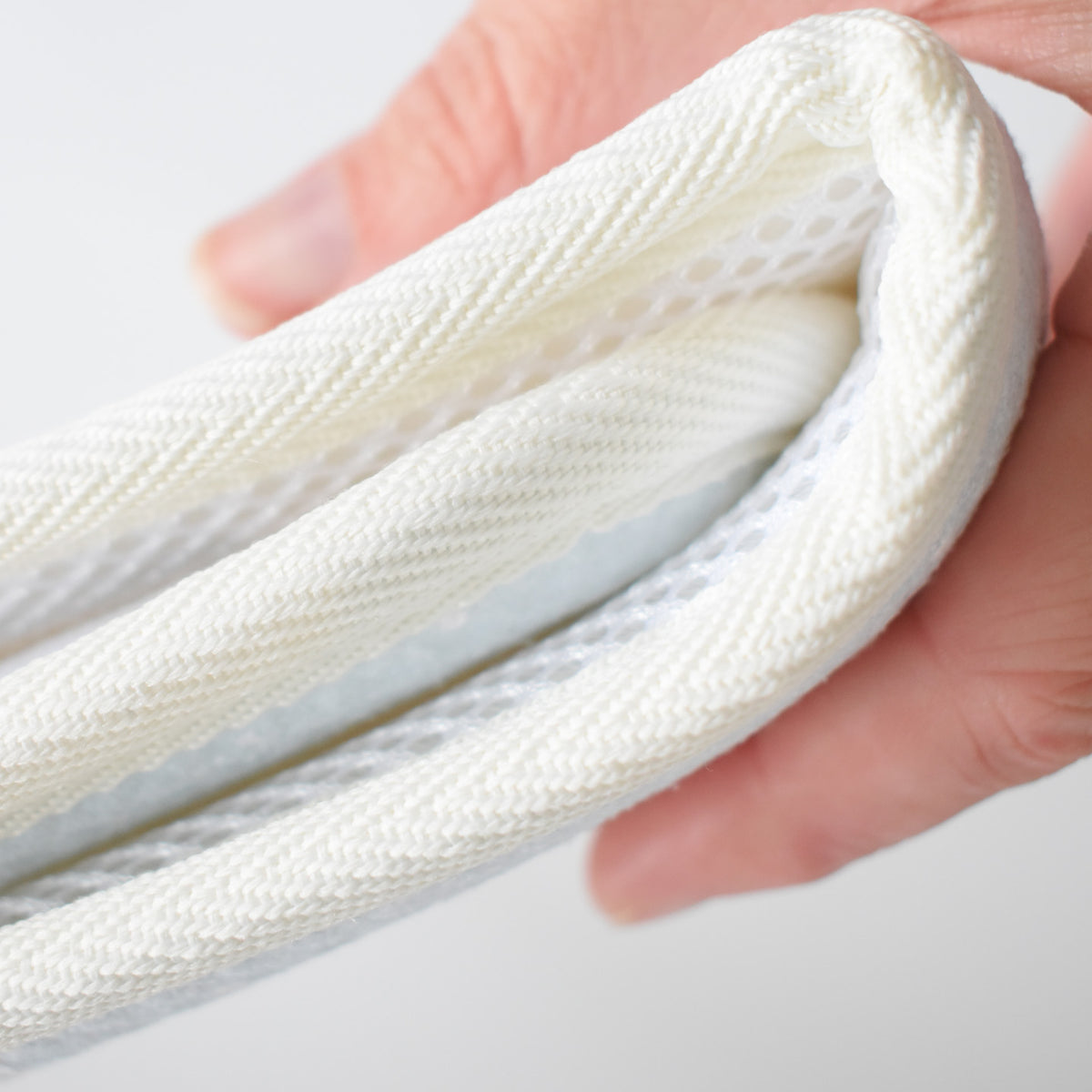 A hand holds the folded edge of a white, cushioned Anywhere Drying Mat, Happy Snowman, which features a textured mesh underside.