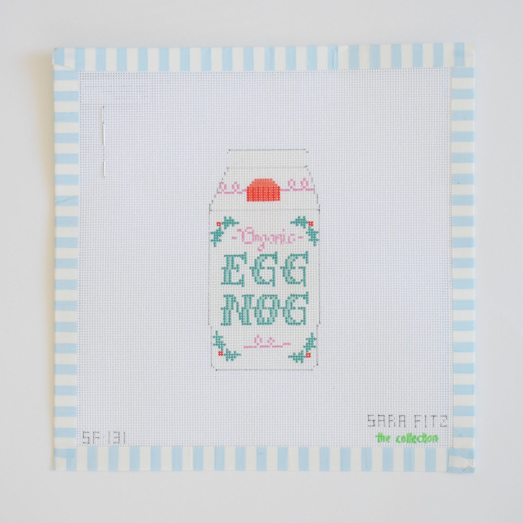 The Eggnog Needlepoint by Sara Fitz features a carton labeled Organic Egg Nog with floral accents, bordered by blue and white stripes on 18 mesh canvas. "Sara Fitz" and other small text appear in the lower corners.