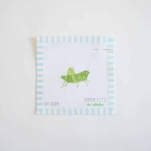 The MINI Grasshopper Needlepoint by Sara Fitz features a stitch-painted 18 mesh canvas with a light green grasshopper design, light blue and white striped edges, and an attached needle. Canvas only; threads not included.
