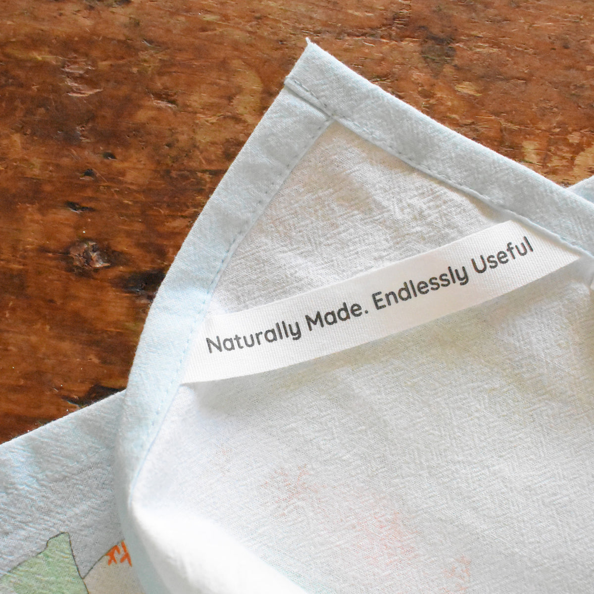A light blue-trimmed Egg Nog Heritage Towel by Sara Fitz featuring a sewn-in label that reads, Naturally Made. Endlessly Useful.