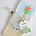 A folded Heritage Towel, Mixing Bowls organic cotton kitchen towel inside a drawstring mesh produce bag with a branded product tag.