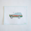 The Holiday Wagon Needlepoint by Sara Fitz showcases a vintage green station wagon with wood paneling, flowers in the back, and a flag on the antenna, bordered by blue and white stripes on 18 mesh canvas.