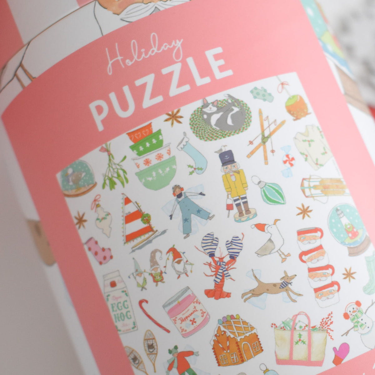 Cylindrical Sara Fitz Holiday Puzzle packaging featuring a pattern of holiday icons, including a nutcracker, lobster, and vintage Santa mug, under the text Holiday PUZZLE.