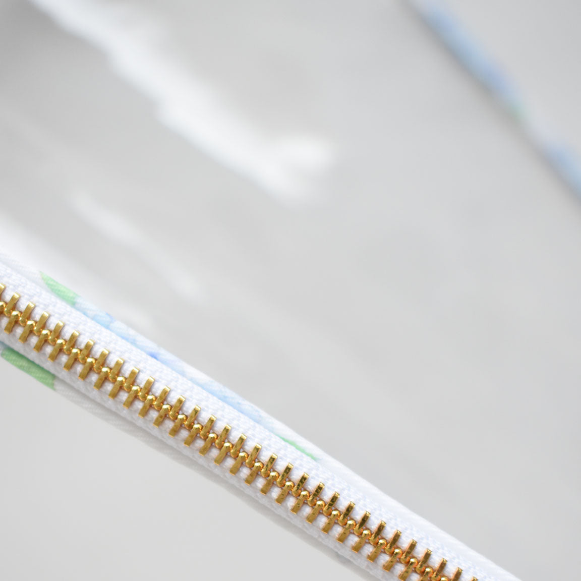 Close-up of the gold metal zipper on the Sara Fitz Hydrangea Project Bag, sewn onto heavyweight white canvas with subtle blue and green accents inspired by hydrangeas, set against a blurred background.