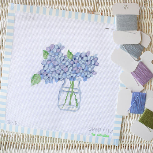 The Sara Fitz Hydrangea Needlepoint features light purple hydrangeas in a glass jar on an 18 mesh canvas, with colored thread cards beautifully arranged for your embroidery project.