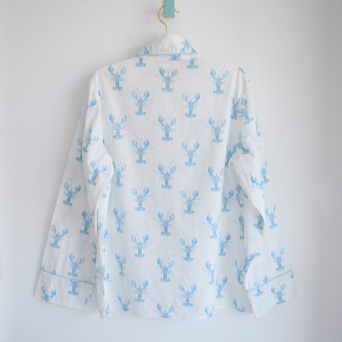 A white long-sleeve button-up shirt hangs on a hanger, adorned with a repeating light blue lobster pattern reminiscent of Sara Fitz style. Shown from the back against a plain white background, this piece pairs perfectly with our Sara Fitz Blue Lobster Pants Pajama Set for a stylish blend of comfort and seaside charm.