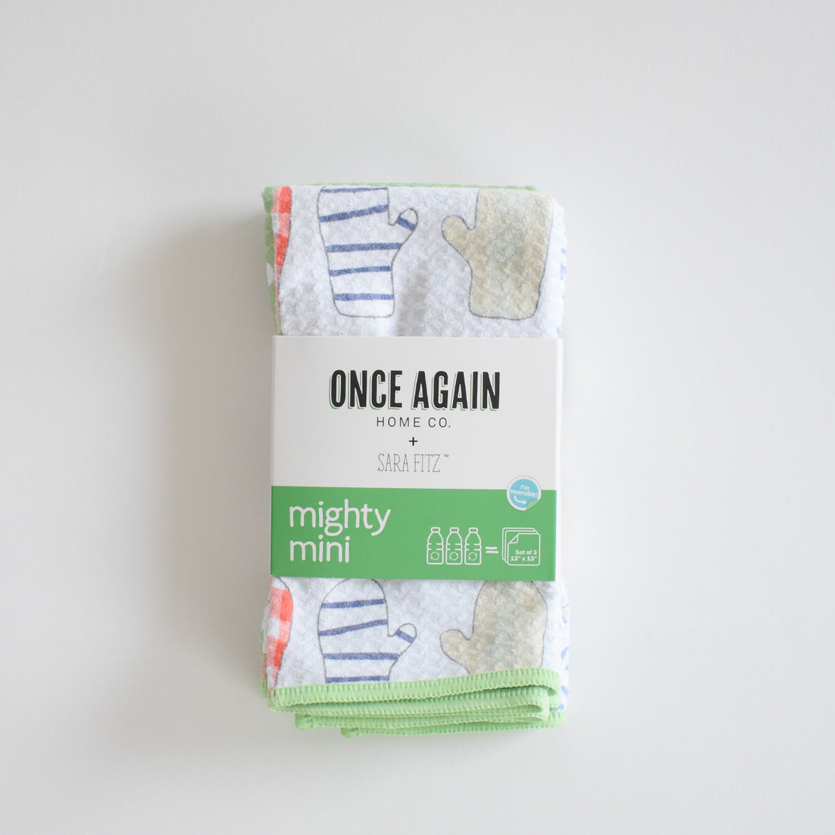 A stack of three Sara Fitz Mighty Mini Towel, Mittens, featuring colorful patterns and wrapped in a paper band.