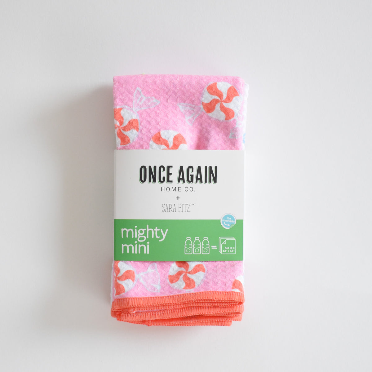 A folded pink Sara Fitz Mighty Mini Towel in Peppermint, patterned with peppermint candies and secured by a paper band, shown as an ultra-absorbent kitchen towel.