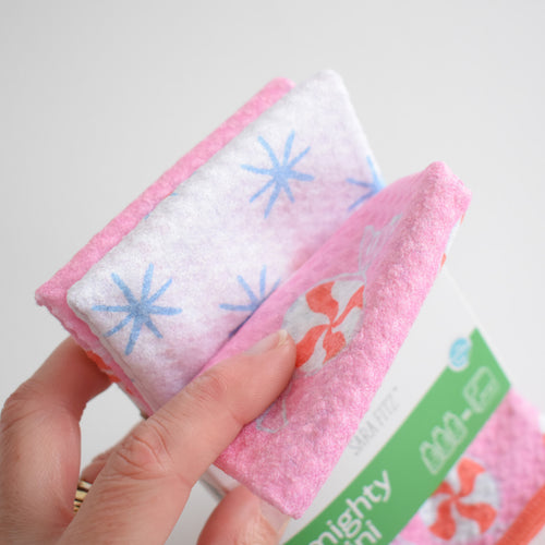 A hand holds a folded Sara Fitz Mighty Mini Towel, Peppermint, featuring a peppermint candy and blue star pattern.