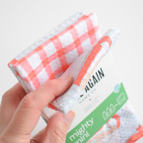 A hand holds a folded red and white checkered Mighty Mini Towel, Santa Mug.