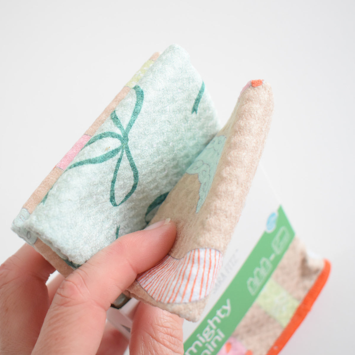 A hand holds a folded Mighty Mini Towel, Stockings, which features a green patterned print.