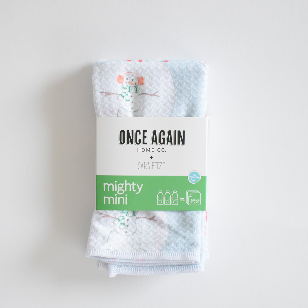 A folded Mighty Mini Towel, Happy Snowman, secured by a paper band labeled Once Again Home Co., showcasing the ultra-absorbent kitchen towel with a snowman print.