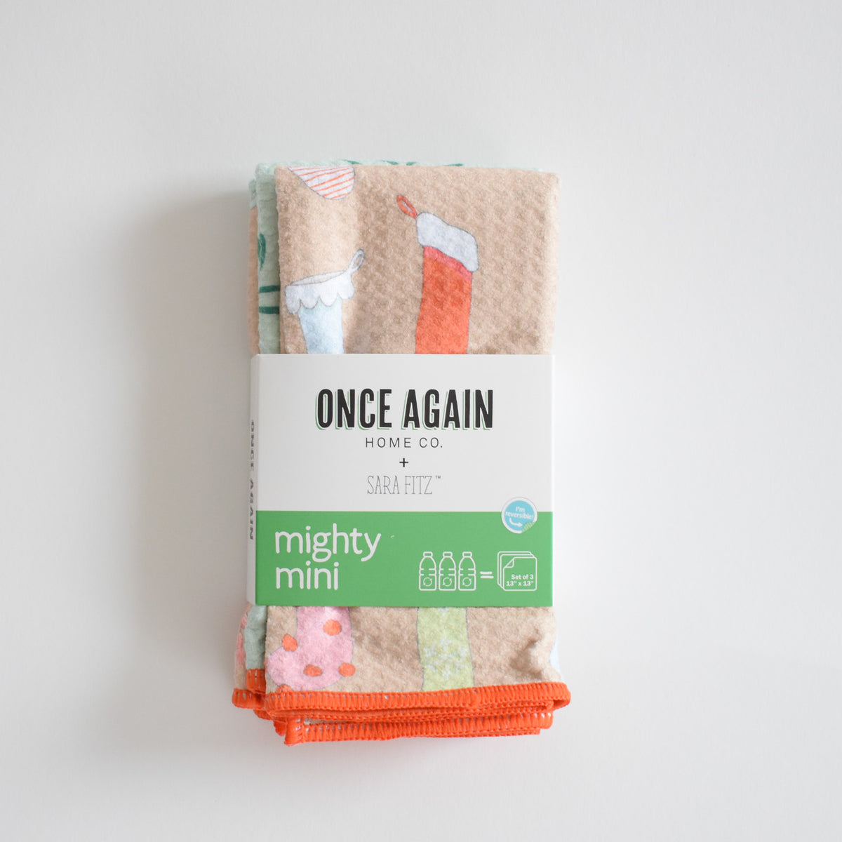 Stacked set of three small, patterned, ultra-absorbent Sara Fitz Mighty Mini Towel, Stockings featuring holiday stocking illustrations, secured with a product label.