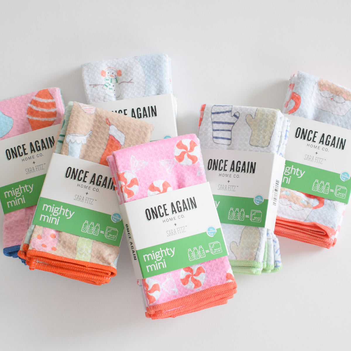 Five folded, ultra-absorbent Mighty Mini Towel, Peppermint kitchen towels with colorful winter and holiday-themed patterns, each wrapped in a paper sleeve.