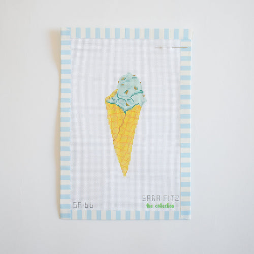 The Mint Gelato Needlepoint by Sara Fitz features a stitch-painted yellow cone with a scoop of mint ice cream, bordered by light blue and white stripes on 18 mesh canvas. "Sara Fitz" is stitched at the lower right.