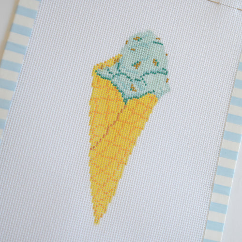 The Mint Gelato Needlepoint by Sara Fitz features a stitch-painted mint chocolate chip ice cream cone with a yellow cone, bordered by blue and white stripes on 18 mesh canvas.