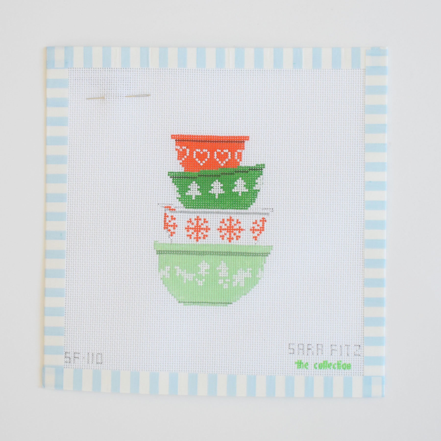The Mixing Bowls Needlepoint by Sara Fitz features four vintage patterned mixing bowls in red and green on white fabric, framed with pale blue and white stripes.
