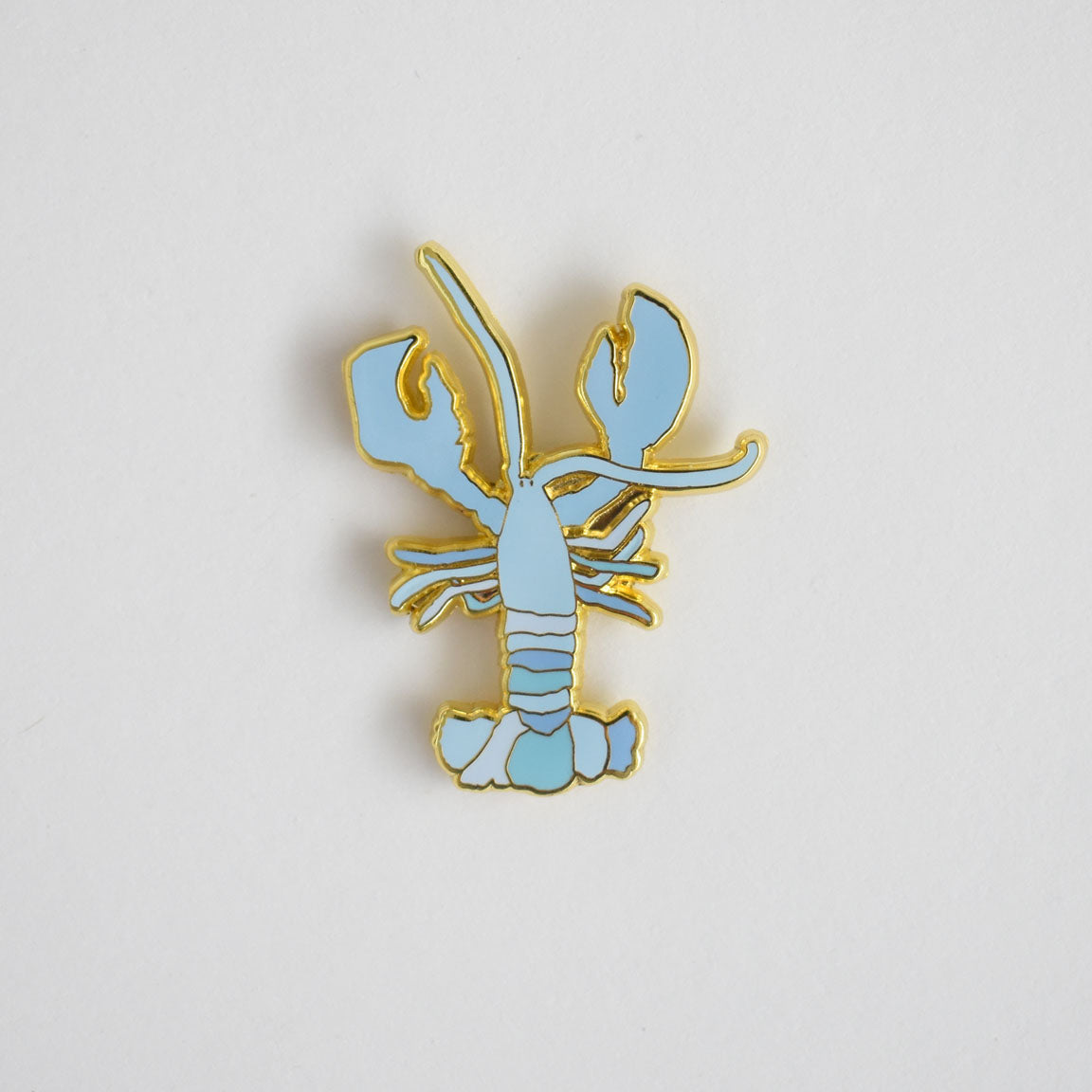 The Blue Lobster Needle Minder by Sara Fitz is a gold-edged enamel pin in the shape of a light blue lobster, shown against a plain white background—making it a charming stitching accessory and the perfect enamel needle minder for your sewing projects.