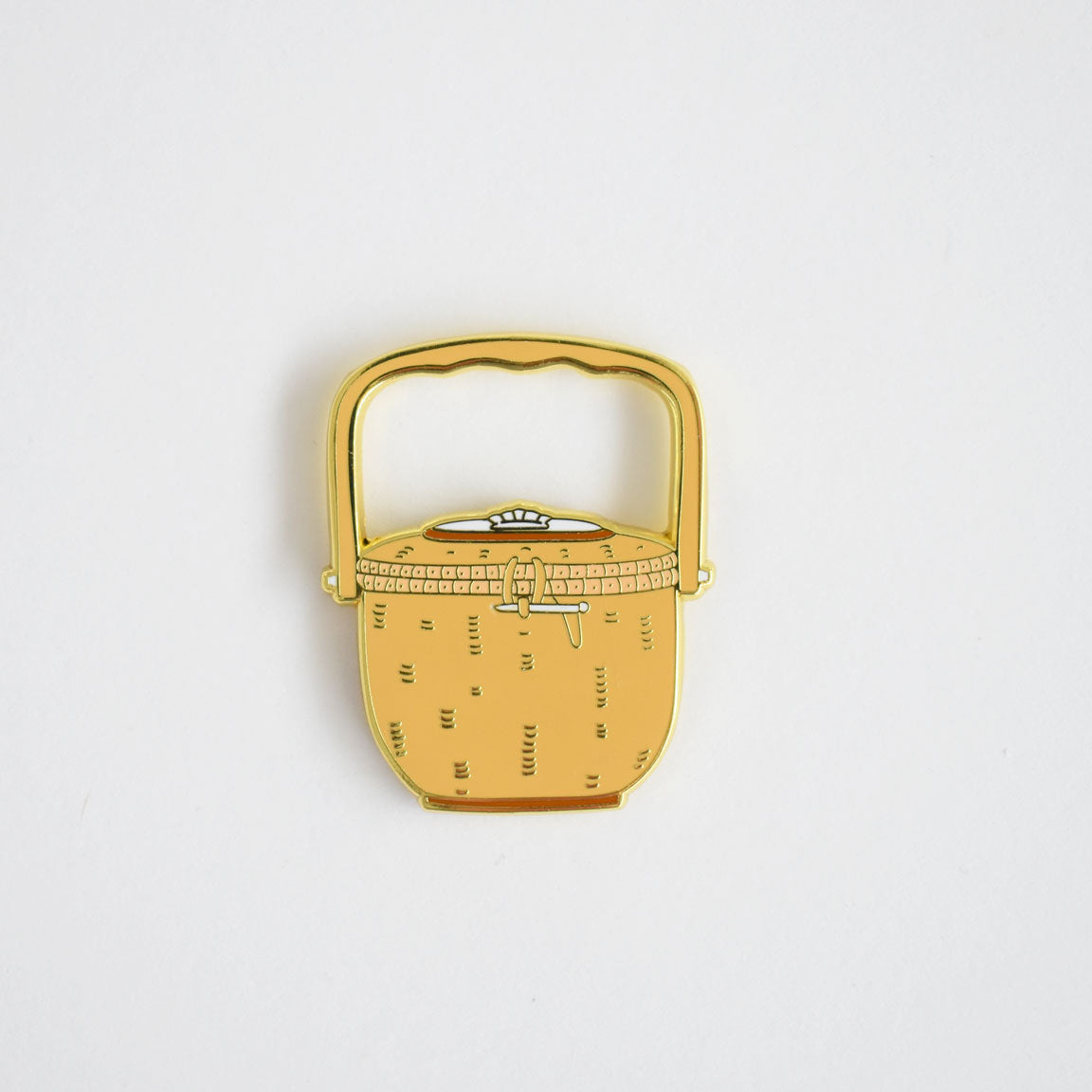The Nantucket Basket Needle Minder by Sara Fitz is a small enamel pin shaped like a yellow woven picnic basket with a curved handle, displayed on a plain white background—perfect as an adorable stitching accessory and enamel needle minder for your next project.