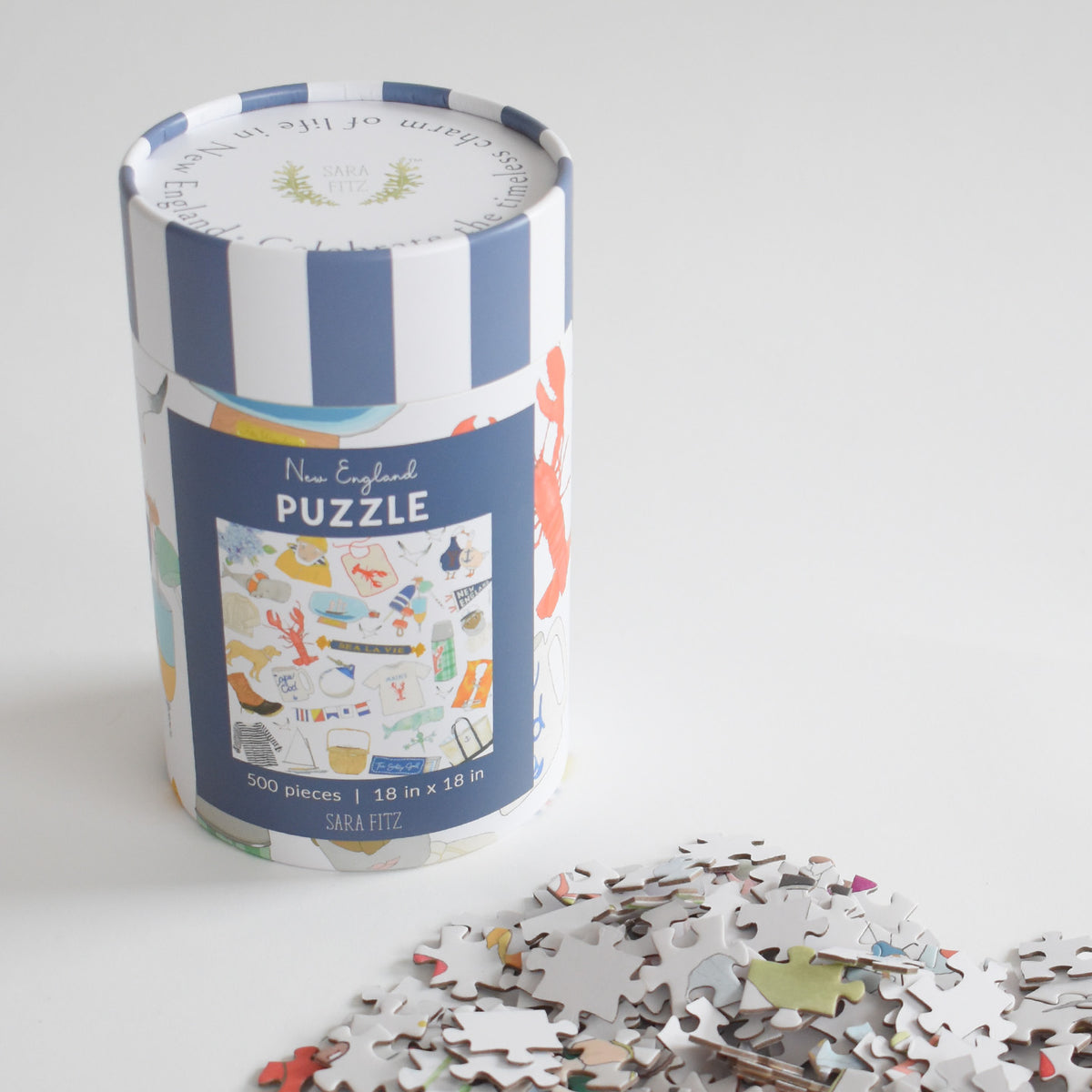 A cylindrical canister containing a 500-piece New England Puzzle, with a pile of loose pieces from the nostalgic collage in the foreground.