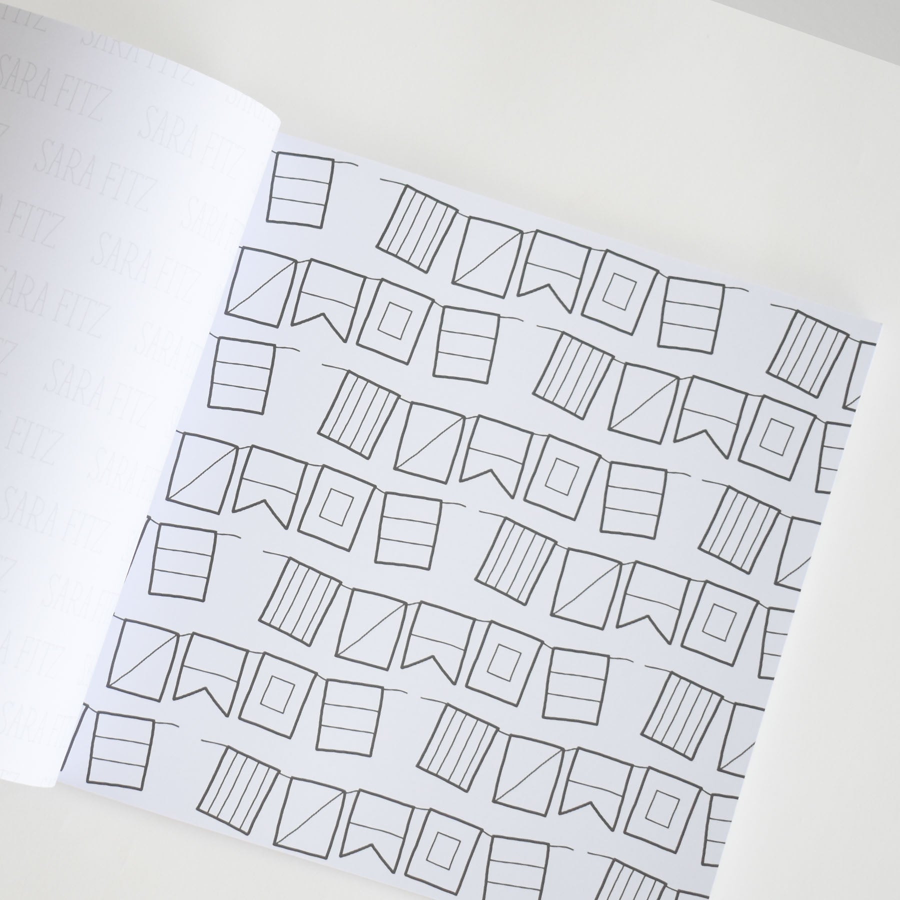 An open notebook displaying pages filled with repeated black line drawings of assorted flag shapes—rectangles, triangles, and squares—neatly arranged in horizontal rows on a white background, makes for a charming addition to any adult coloring book collection or as part of the Sara Fitz Coloring Book New England series.