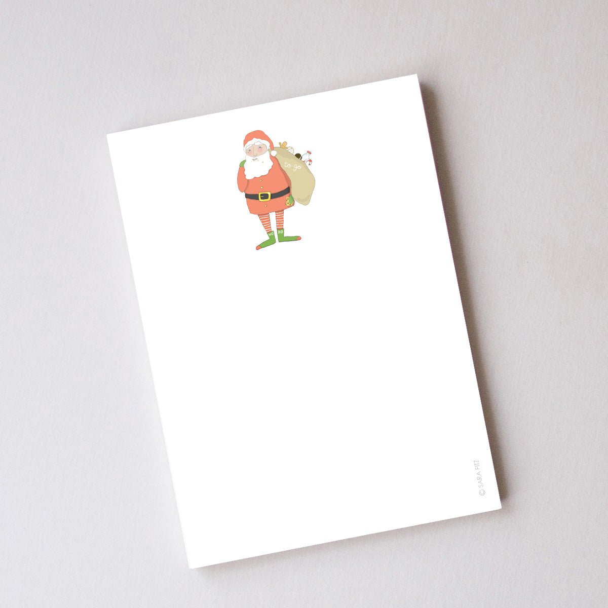 White Santa Fitz notepad featuring an illustration of Santa Claus carrying a sack over his shoulder, with unlined pages.