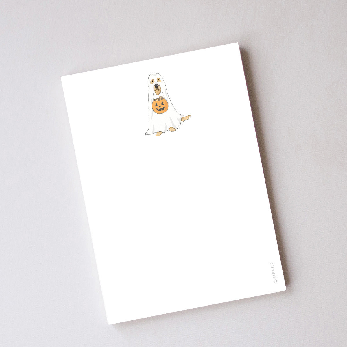Introducing the Trick or Treat Pup Notepad by Sara Fitz—a charming illustrated notepad featuring a delightful dog dressed as a ghost holding a pumpkin-shaped bucket at the top of each page. Made in the USA, this notepad offers unlined pages with ample space for your notes and doodles, while the rest of the sheet remains blank to let your creativity shine.